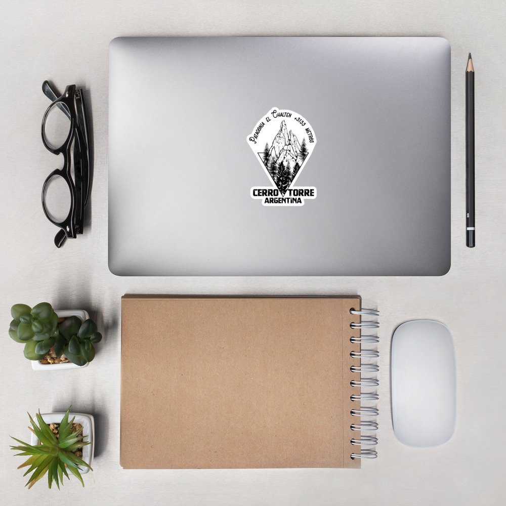 Pegatina Cerro Torre sobre ordenador en escritorio con gafas y cuaderno