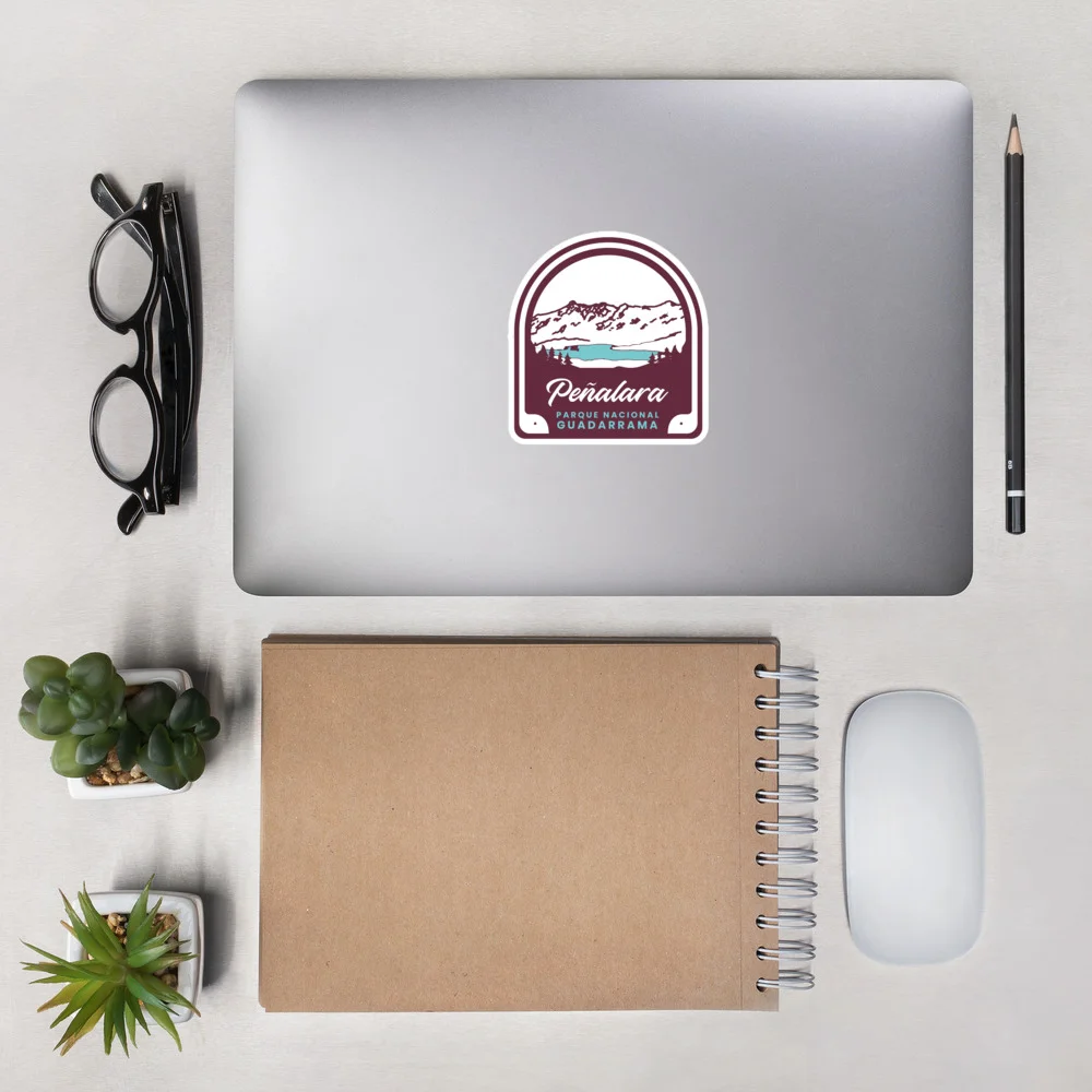 Pegatina Peñalara sobre ordenador en escritorio con gafas y cuaderno