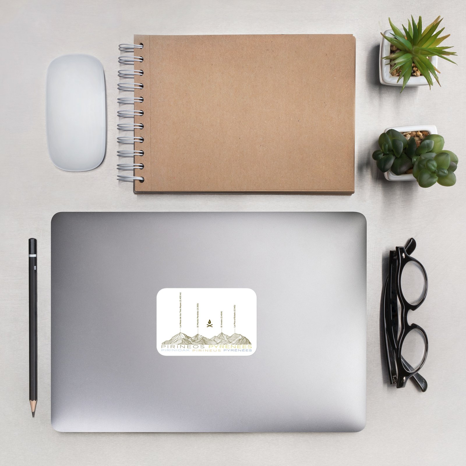 Pegatina de los Pirineos con relieve montañoso sobre fondo de ordenador en escritorio, con gafas y cuaderno.
