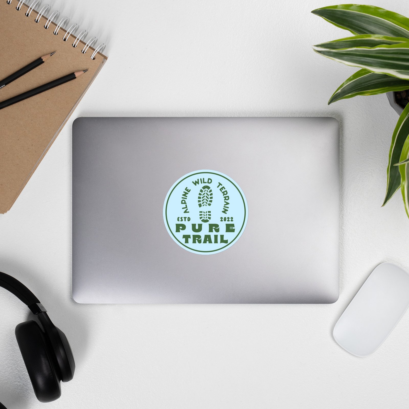 Pegatina de vinilo con diseño de montaña en laptop junto a planta y accesorios.