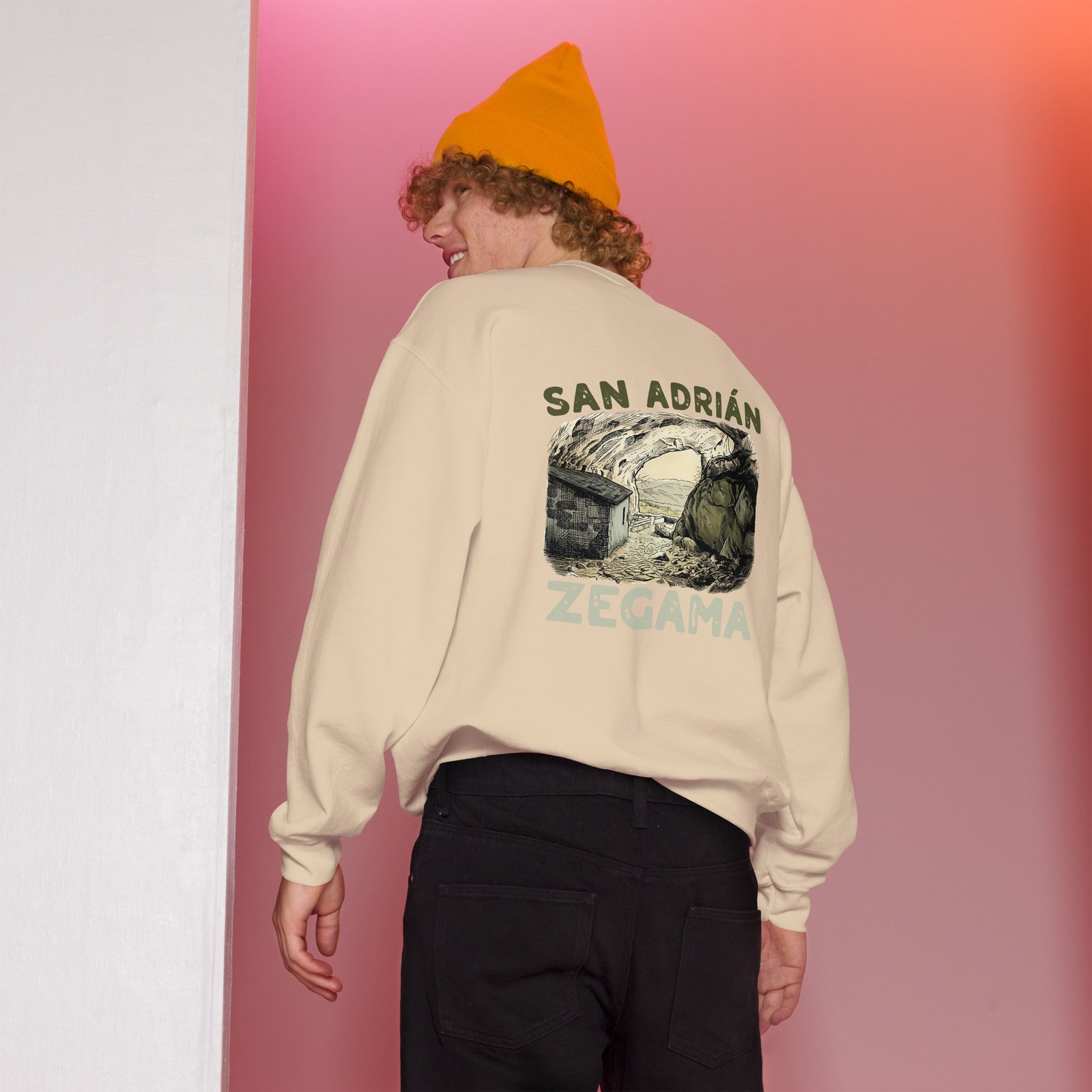 Hombre con sudadera beige y gorro naranja mostrando diseño de San Adrián Zegama.